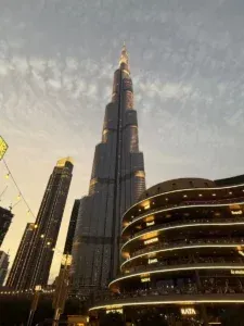 Vue en plongée du Burj Khalifa illuminé s'élevant dans un ciel de crépuscule, avec un bâtiment commercial à plusieurs niveaux et des enseignes lumineuses au premier plan, prise à Dubaï le 6 mars 2026