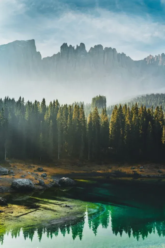 Paysage de montagne sauvage avec une forêt de pins et un lac aux eaux turquoises reflétant les sommets.